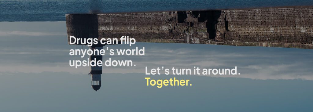Upside down picture of a lighthouse and sea wall. The words say 'Drugs can flip anyone’s world upside down. Let’s turn it around. Together.'